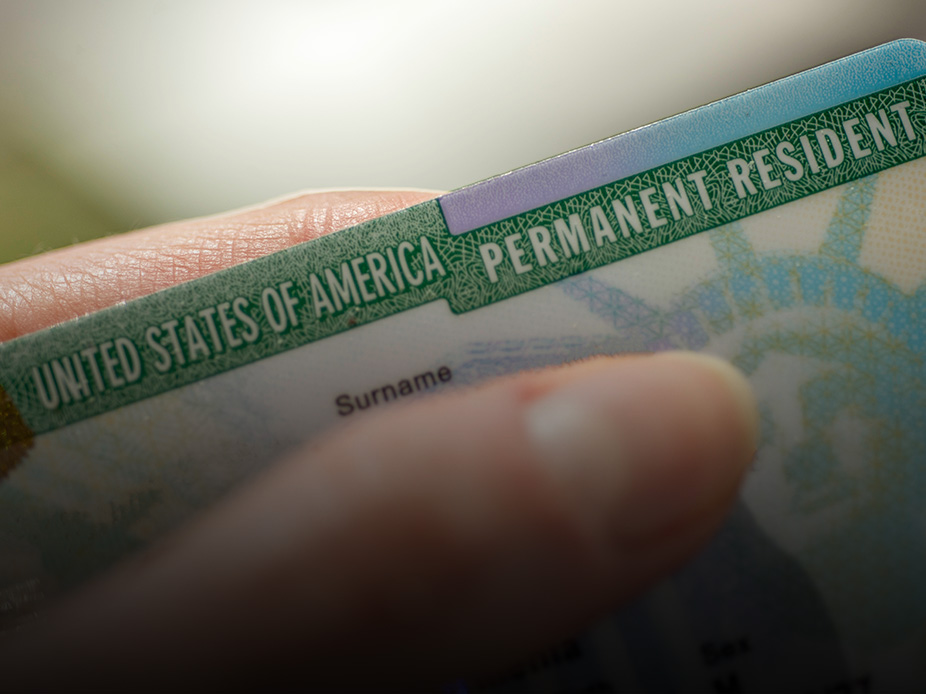 A hand holding a United States of America Permanent Resident green card.